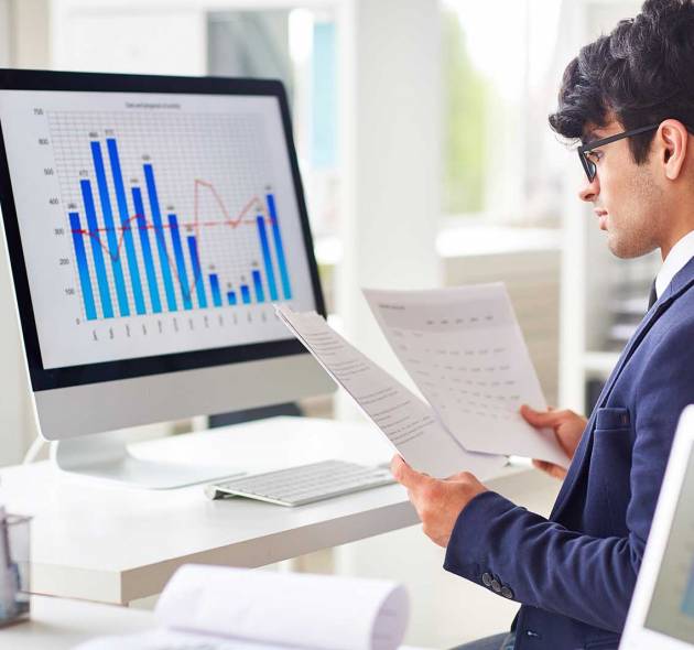 Businessman looking through papers by workplace and analyzing statistics